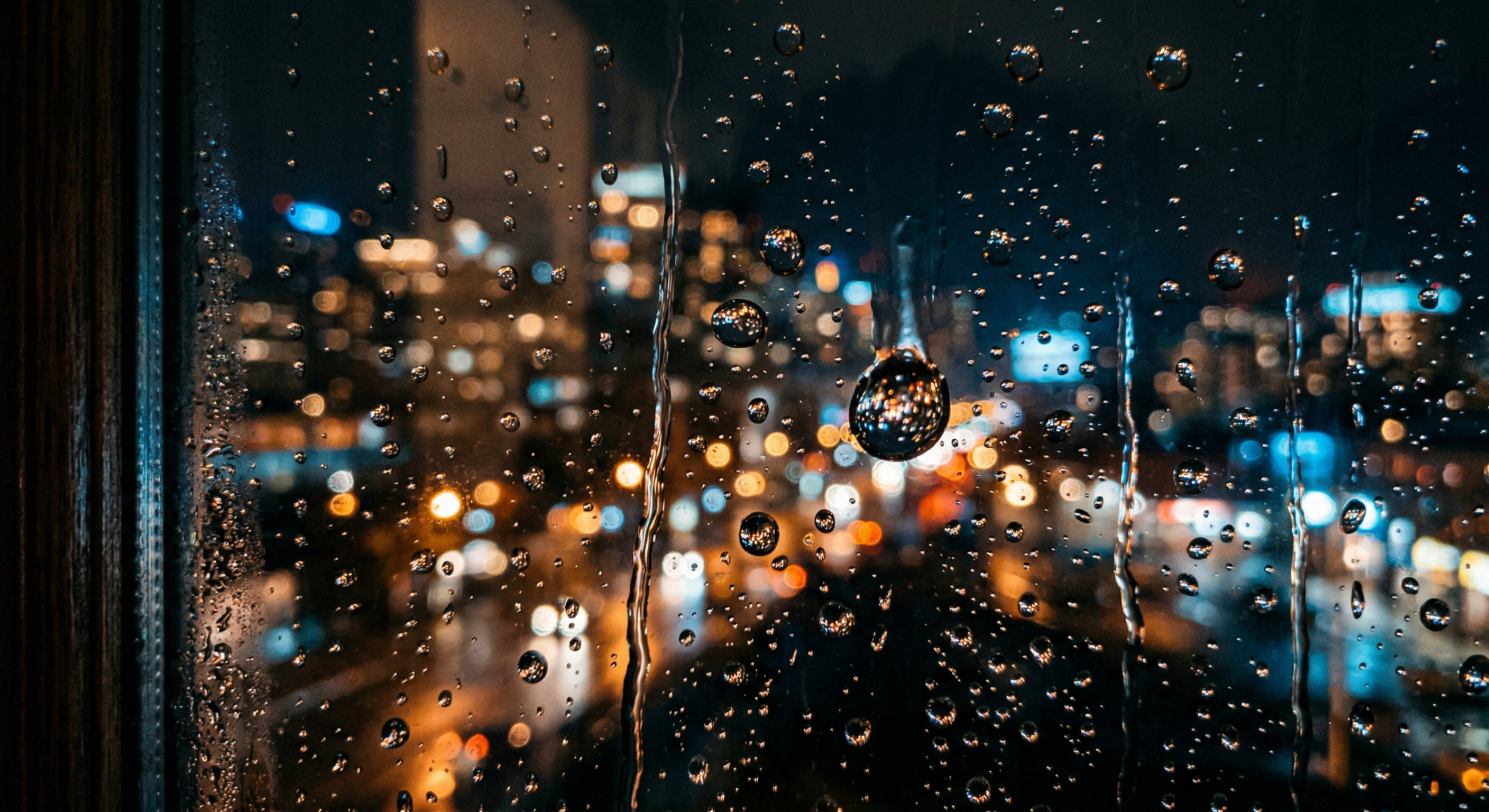 Rain on a window at night, city lights refracted through droplets