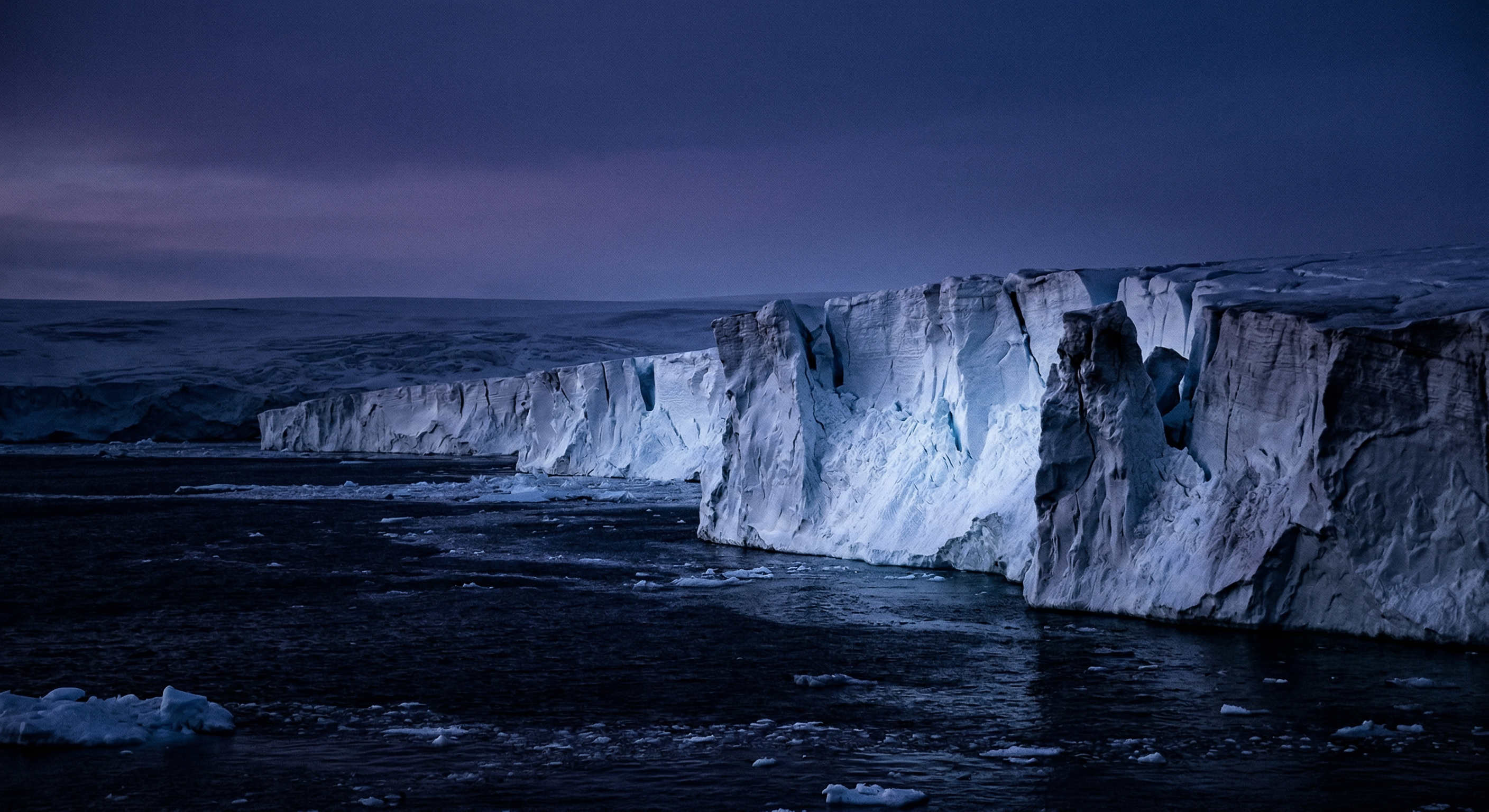 The edge of Antarctica at twilight, ice meeting deep navy sea