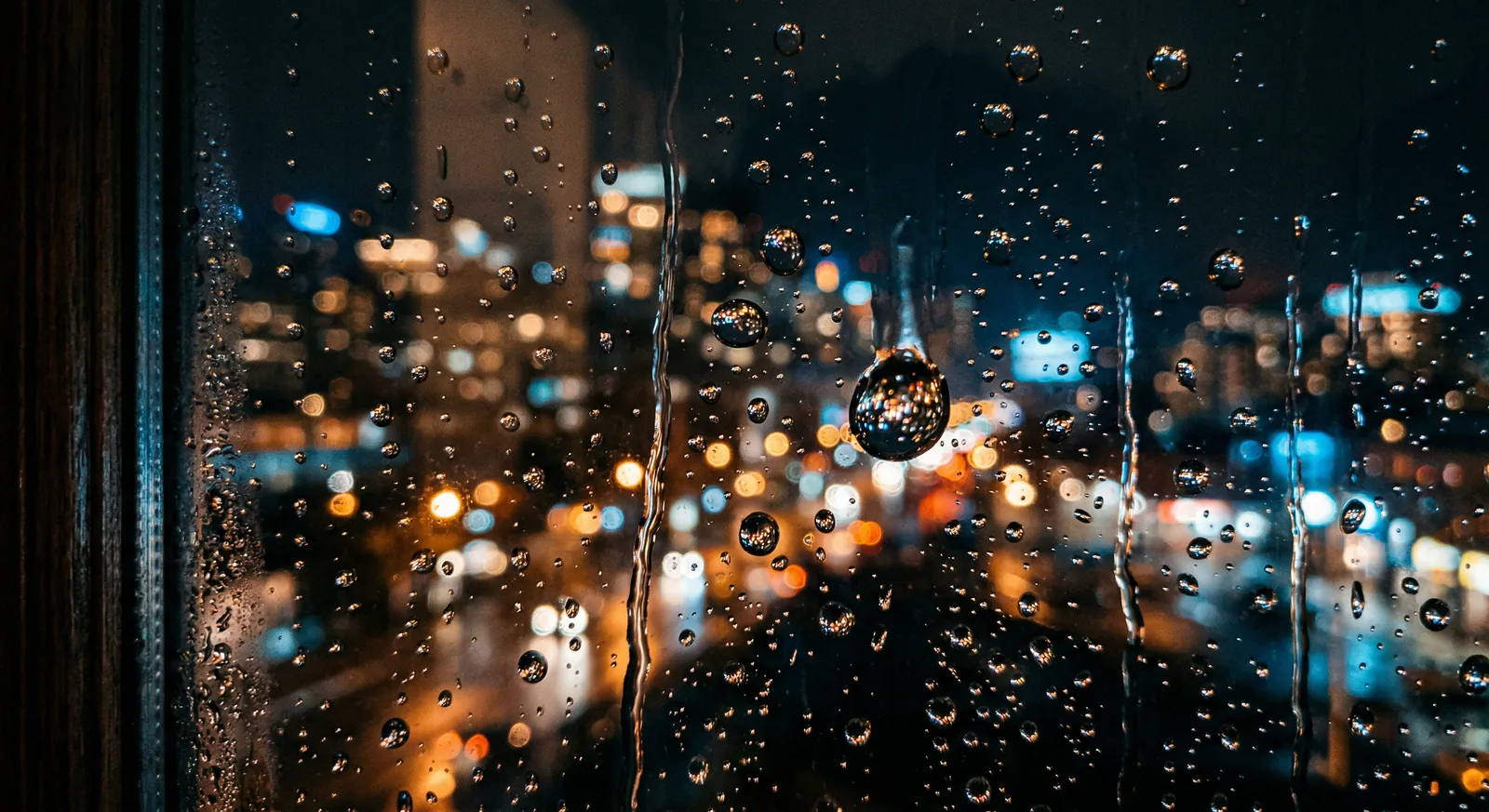 City lights blur through raindrops on a dark window.
