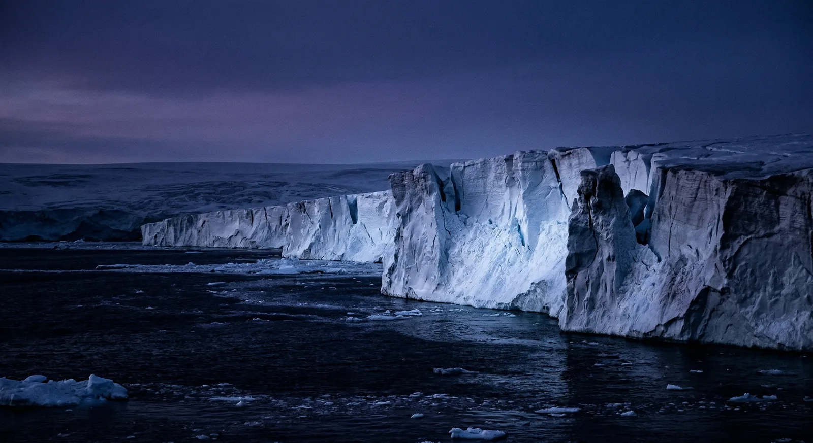An imagined Antarctic ice shelf meets dark sea beneath a twilight sky.
