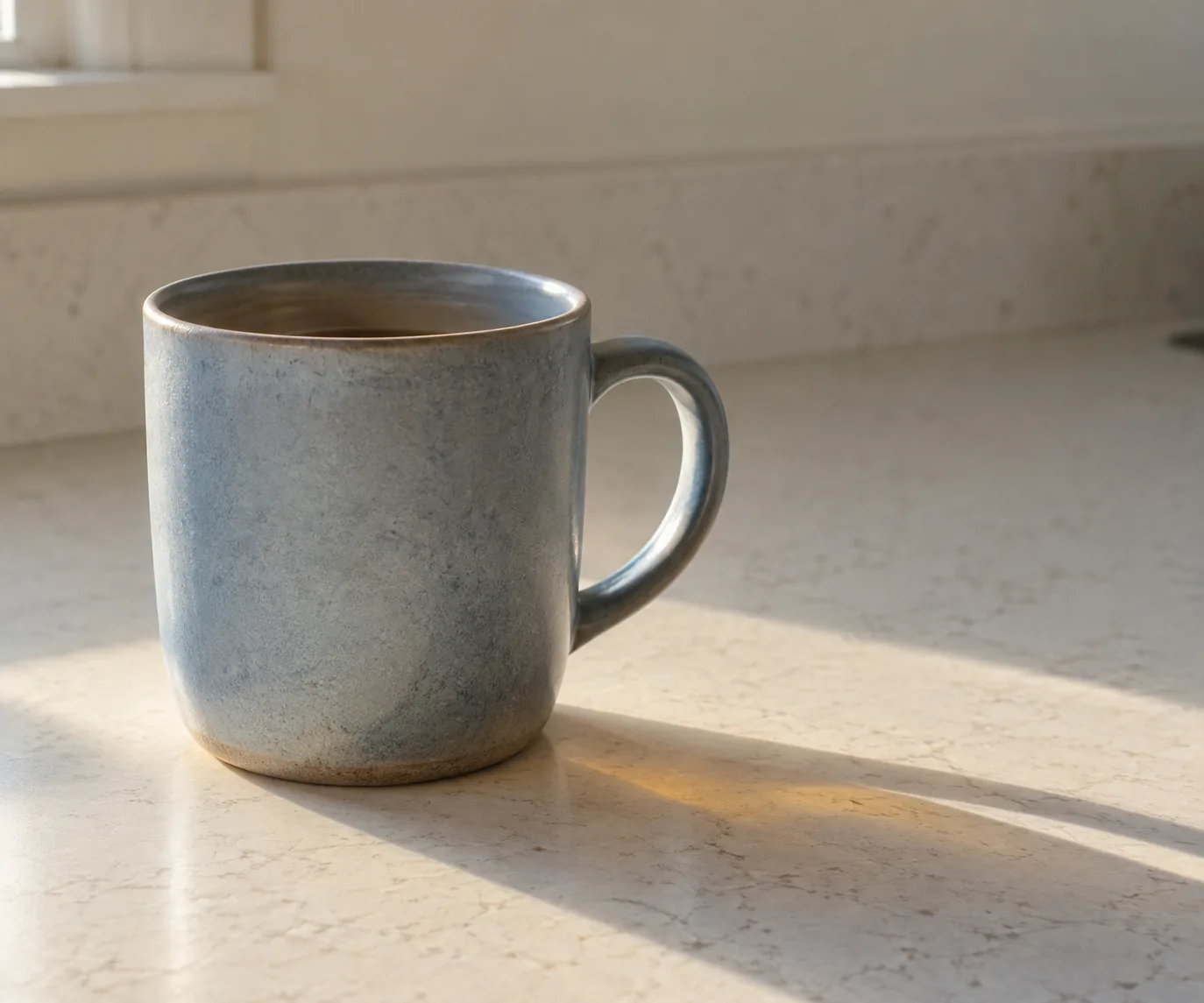 A ceramic mug resting on a kitchen counter in soft light, with a warm shadow beside it.