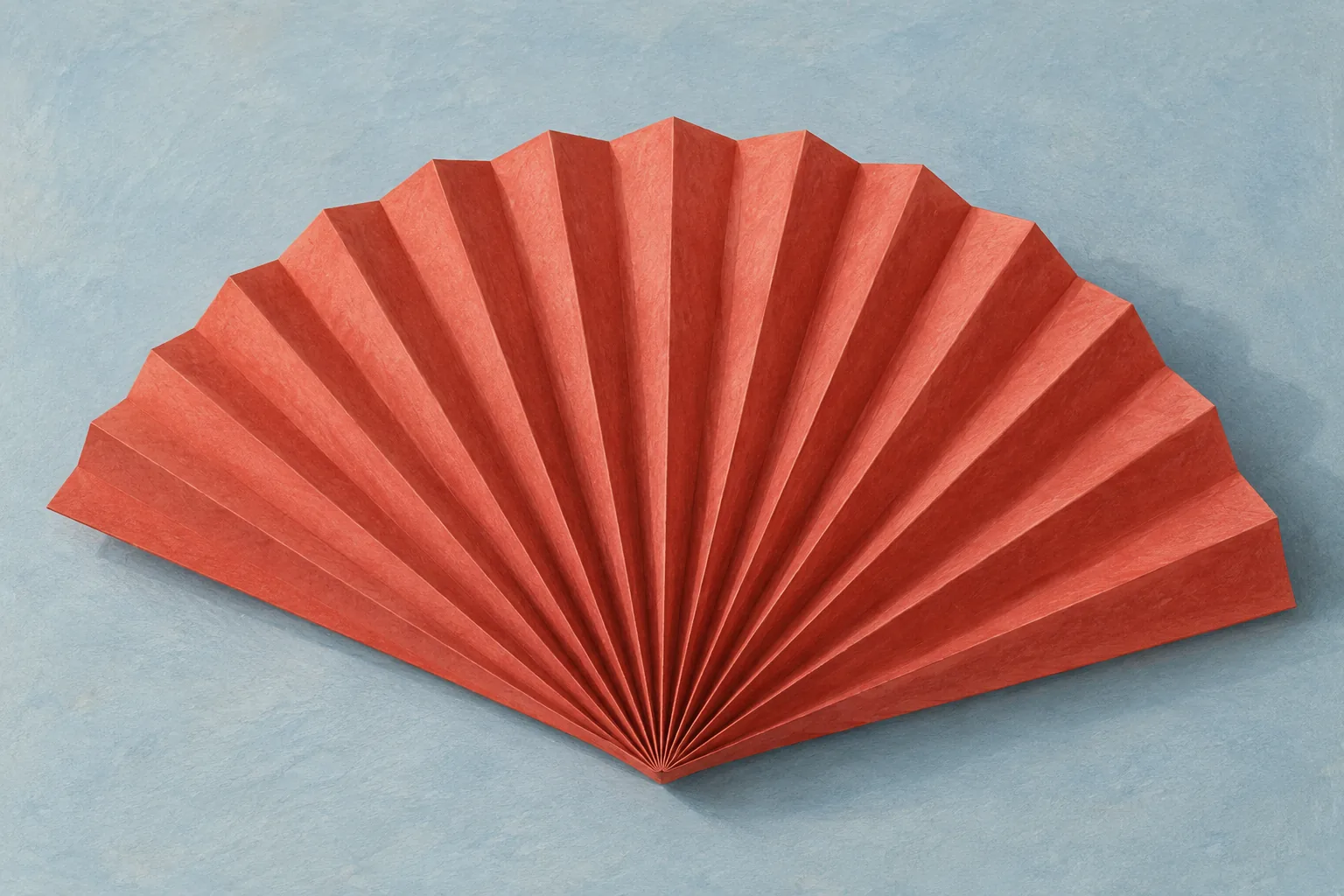 A coral-red accordion-fold paper fan opens across a pale blue-gray surface, its ridges and valleys catching soft light.